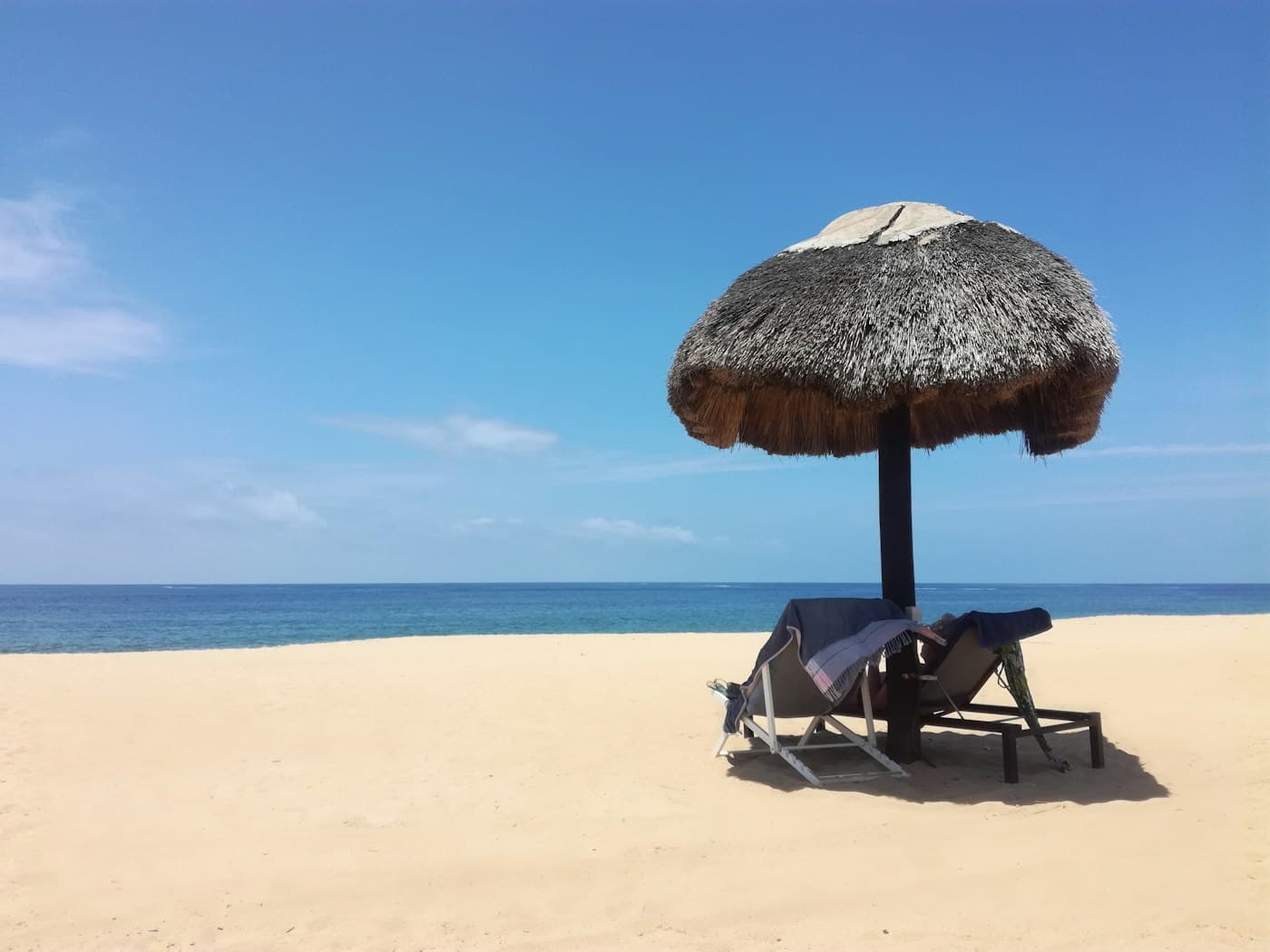 Cadeira de praia junto a um guarda-sol de palha na areia da Restinga, no Lobito