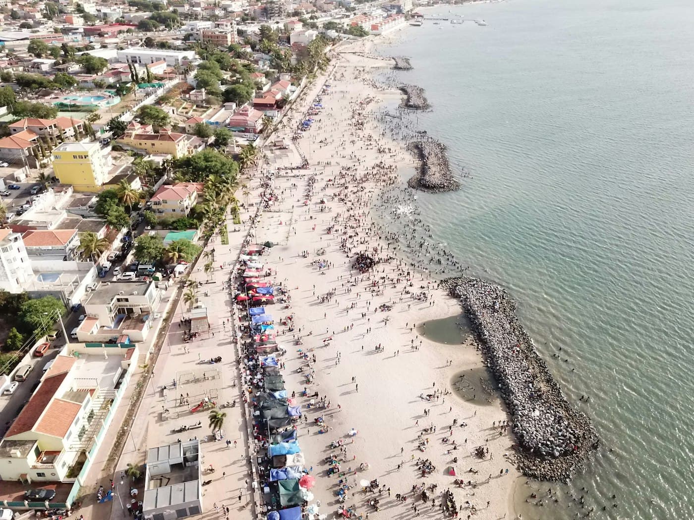 Vista aérea de uma praia cheia de gente, junto a casas, em Luanda